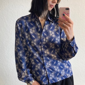 Pu&ograve; includere: Una camicia a maniche lunghe blu e bianca con colletto e chiusura con bottoni.