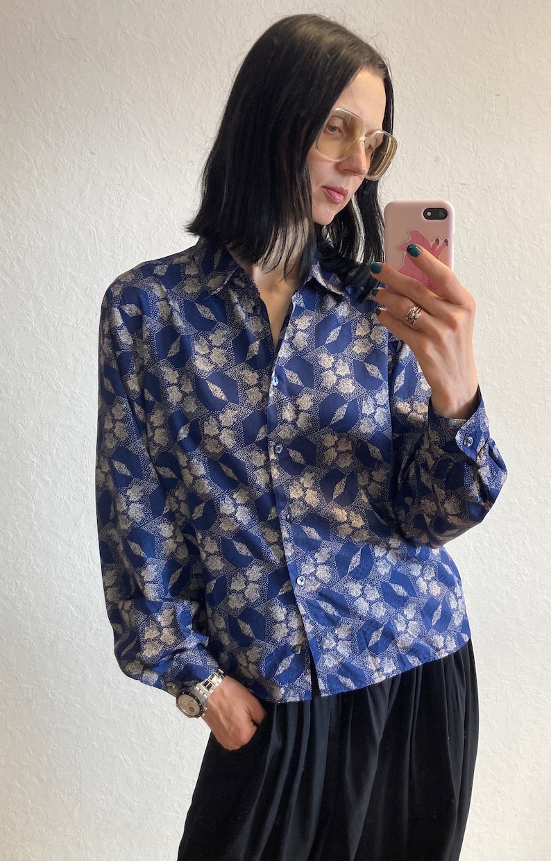 Pu&ograve; includere: Una camicia a maniche lunghe blu e bianca con colletto e chiusura con bottoni.