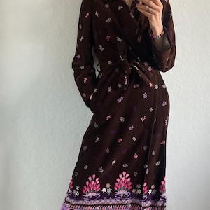 May include: A long, brown robe with a floral pattern and a tie waist. The robe features a colorful floral and paisley design at the hemline. The robe is made of a soft, velvety material, perfect for lounging.