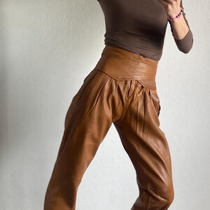 May include: A person wearing a brown long-sleeve shirt and high-waisted, brown leather pants. The person is also wearing black and white sneakers with a leopard print design.