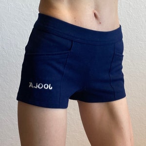 May include: Navy blue athletic shorts with two front pockets and a white embroidered logo that reads "A.JOOL". The shorts are made of a stretchy material and have a fitted design.