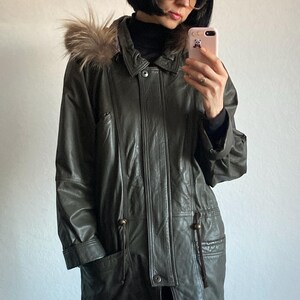 May include: Olive green leather jacket with a fur-trimmed hood. The jacket features a button-down front, pockets, and a drawstring waist. The jacket is a classic outerwear piece.