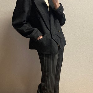 May include: A black blazer with a double-breasted closure and a white lace top underneath. The person is wearing black and white striped pants and black shoes.