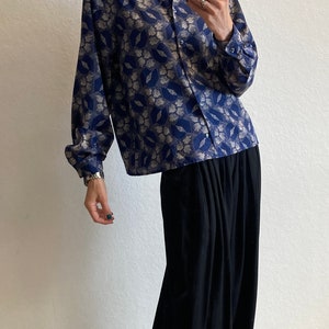 Pu&ograve; includere: Una donna indossa una camicia a maniche lunghe con motivo blu e argento, una gonna maxi nera e scarpe di tela a righe bianche e nere.