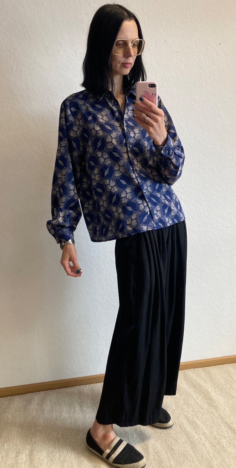 Pu&ograve; includere: Una donna indossa una camicia a maniche lunghe con motivo blu e argento, una gonna maxi nera e scarpe di tela a righe bianche e nere.