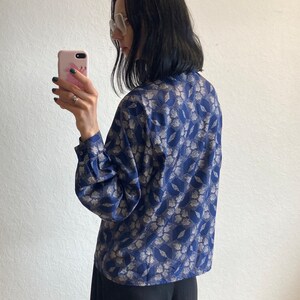 Pu&ograve; includere: Una blusa blu e bianca con motivo a fantasia, maniche lunghe e chiusura con bottoni sul davanti.