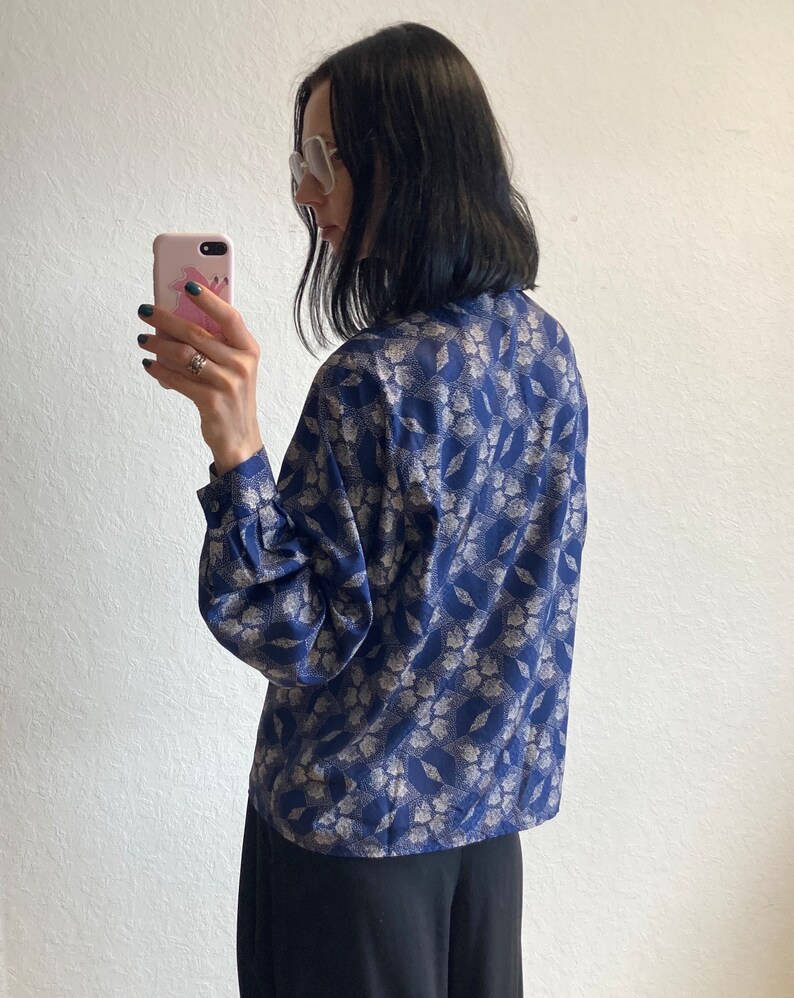 Pu&ograve; includere: Una blusa blu e bianca con motivo a fantasia, maniche lunghe e chiusura con bottoni sul davanti.