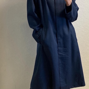 May include: A woman wearing a dark blue long coat, black pants, and leopard print shoes. She is holding a cell phone in her hand.