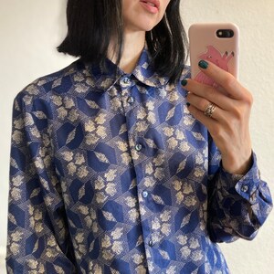 Pu&ograve; includere: Una camicia a maniche lunghe con un motivo blu e bianco, un colletto e una chiusura con bottoni.