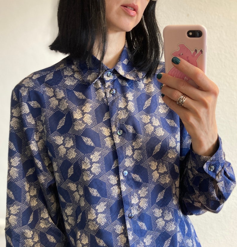 Pu&ograve; includere: Una camicia a maniche lunghe con un motivo blu e bianco, un colletto e una chiusura con bottoni.