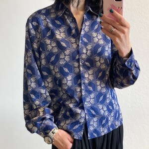 Pu&ograve; includere: Una camicia a maniche lunghe con bottoni e colletto, con motivo blu e bianco. La camicia presenta un motivo geometrico con accenti bianchi su uno sfondo blu scuro.