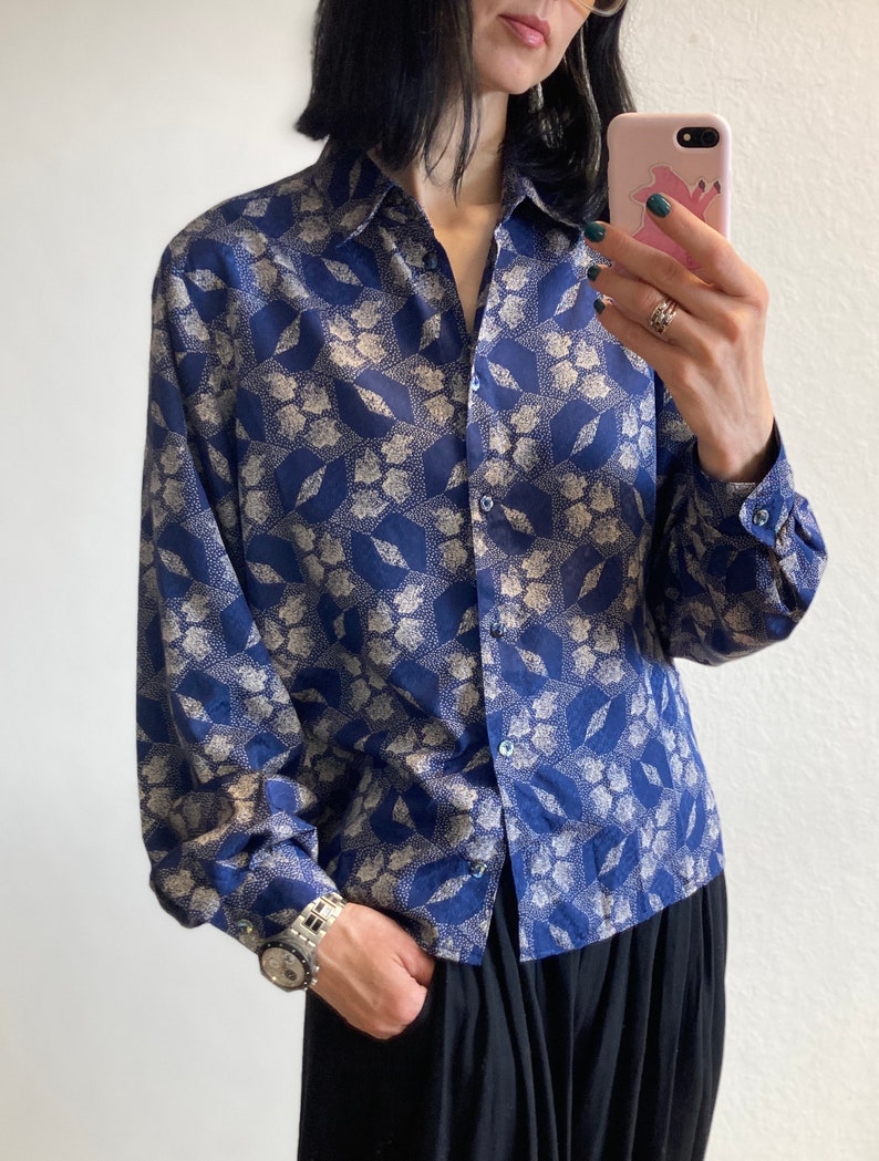 Pu&ograve; includere: Una camicia a maniche lunghe con bottoni e colletto, con motivo blu e bianco. La camicia presenta un motivo geometrico con accenti bianchi su uno sfondo blu scuro.