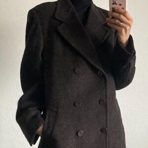 May include: A dark brown double-breasted coat with a classic design. The coat features a notched lapel, two rows of buttons, and a tailored fit. The coat is made of a textured fabric and has pockets.
