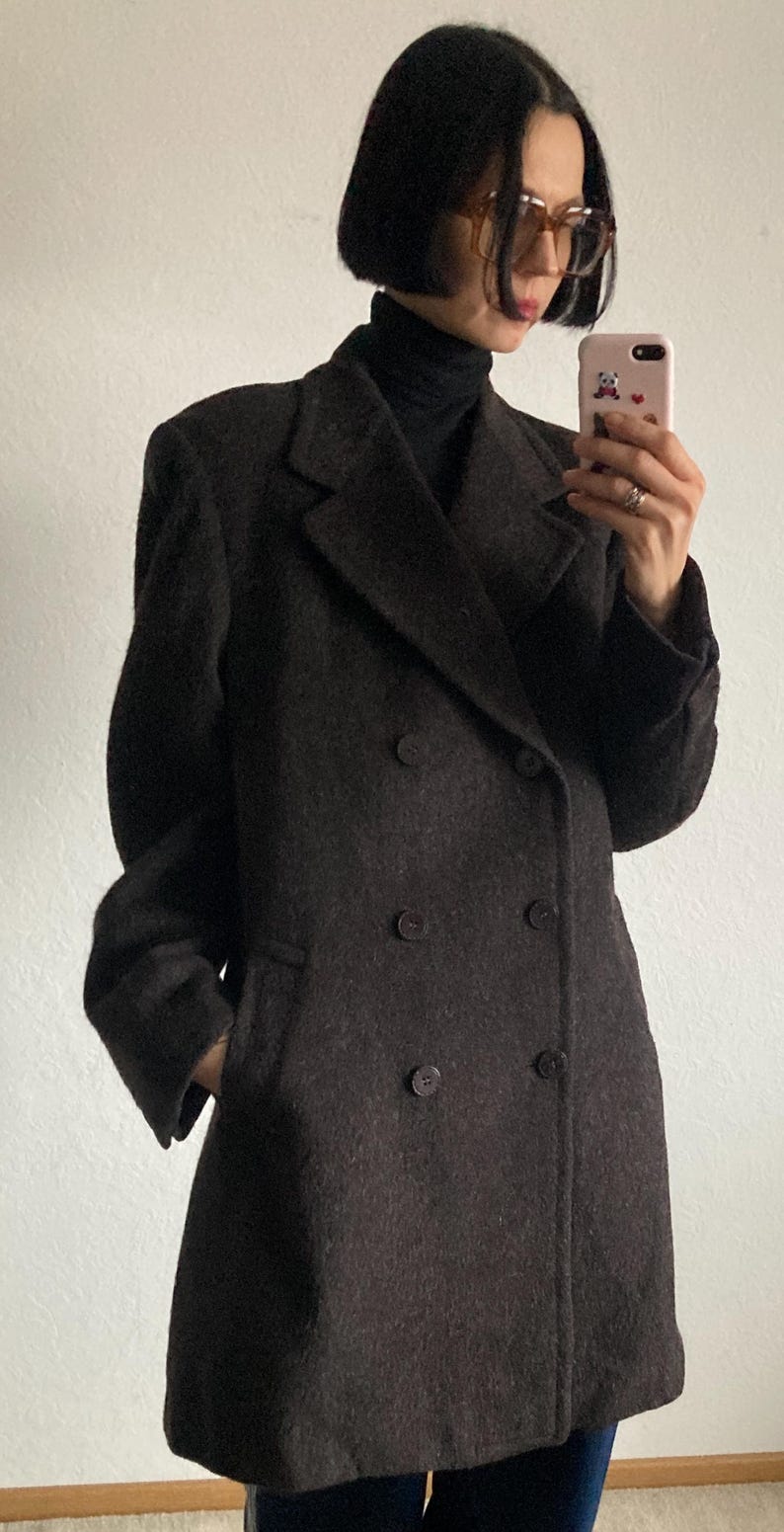 May include: A dark brown double-breasted coat with a classic design. The coat features a notched lapel, two rows of buttons, and a tailored fit. The coat is made of a textured fabric and has pockets.