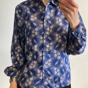 Pu&ograve; includere: Una camicia a maniche lunghe blu e bianca con motivo a fiori e chiusura con bottoni. La camicia ha un motivo geometrico con fiori bianchi su sfondo blu.