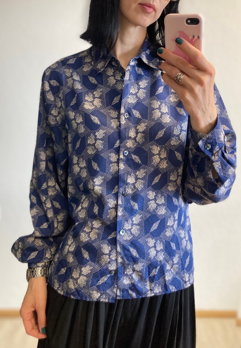 Pu&ograve; includere: Una camicia a maniche lunghe blu e bianca con motivo a fiori e chiusura con bottoni. La camicia ha un motivo geometrico con fiori bianchi su sfondo blu.