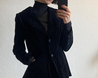 May include: A black velvet blazer with a fitted silhouette and a single button closure. The blazer has a pointed collar and a single pocket on the left side.