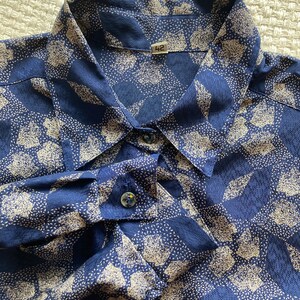 Pu&ograve; includere: Una camicia abbottonata blu e bianca con motivo, colletto e maniche lunghe. La camicia ha un'etichetta di taglia che dice "42".