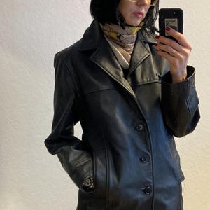 May include: A black leather jacket with a button closure and two pockets. The jacket has a collar and a slightly fitted silhouette.