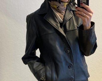 May include: A black leather jacket with a button closure and two pockets. The jacket has a collar and a slightly fitted silhouette.