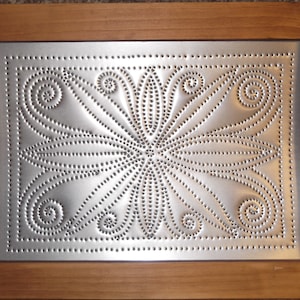 May include: A silver metal wall decor with a raised, embossed floral design. The decor is framed in a natural wood frame.