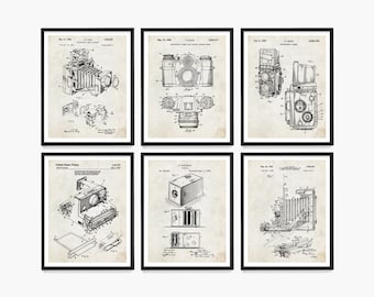 Op de afbeelding: Een set van zes vintage camera patent prints. Elke print toont een zwart-witte illustratie van een ander cameradesign. De prints zijn ingelijst in zwarte frames en hebben een witte achtergrond.
