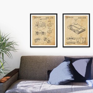 Peut inclure: Deux impressions encadr&eacute;es noires de dessins de brevets vintage pour une manette de jeu vid&eacute;o et une console de jeu vid&eacute;o. Les dessins sont sur un fond beige avec des lignes noires.