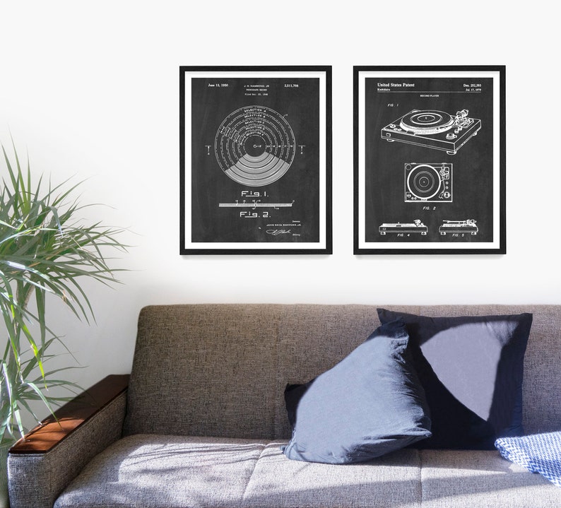 May include: Two black and white vintage patent drawings of a record player. The first drawing shows a diagram of a record player turntable. The second drawing shows a side view of a record player. The drawings are framed in black frames and are hanging on a white wall.