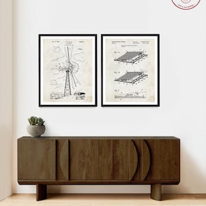 May include: Two black and white vintage patent drawings framed in black frames. The left drawing shows a windmill design. The right drawing shows a solar panel design. The drawings are hanging on a white wall above a dark brown wooden cabinet.