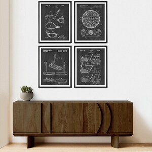 May include: Set of four black and white vintage patent prints featuring golf equipment. The prints depict a golf club, a golf ball, and a golf putter. The prints are framed and displayed on a wall above a dark brown wooden cabinet.