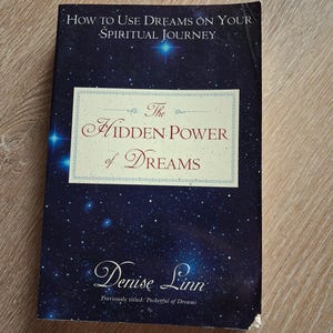 Peut inclure: Un livre intitulé "The Hidden Power of Dreams" de Denise Linn. La couverture présente un fond bleu foncé avec un motif de nuit étoilée. Le texte "How to Use Dreams on Your Spiritual Journey" est en haut.