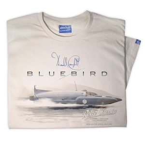 Puede incluir: Una camiseta beige con una ilustración azul y blanca de un barco que rompe el récord de velocidad en el agua, "Bluebird", con la firma de Donald Campbell. El texto "Retro Classic Campbell Heritage Collaboration 1958 Water Speed Record" está impreso debajo de la ilustración.