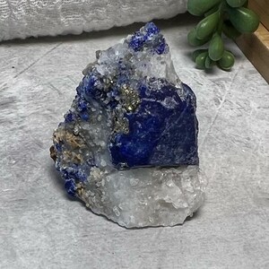 May include: A blue and white crystal cluster with a large blue crystal in the centre. The crystal is surrounded by smaller white crystals and some gold-coloured pyrite.