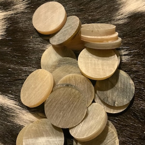 May include: A collection of light-colored, round, flat objects with a natural, textured appearance. The objects are stacked and scattered, suggesting they are game pieces or decorative elements. The background is a dark, patterned surface.