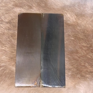 May include: Two rectangular sharpening stones, one brown and one black, side by side on a light brown fuzzy surface.