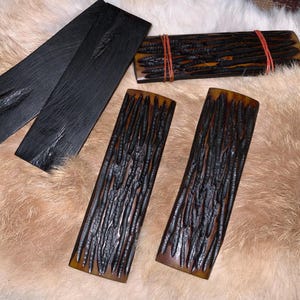 May include: Four pieces of black and brown wood, possibly for knife handles, with a wood grain pattern. The wood is arranged on a white fur surface.