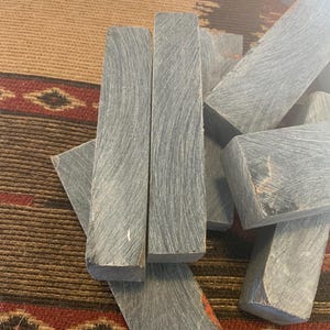 May include: A pile of gray and black wood blanks, likely for knife handles, on a patterned rug.
