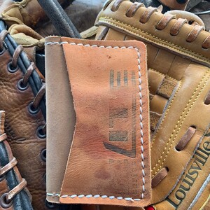 Cartera de cuero con forma de guante de béisbol. Fabricada con guantes de béisbol reciclados y piel de novillo de primera calidad. Tiene 3 bolsillos. Fabricada en Estados Unidos.