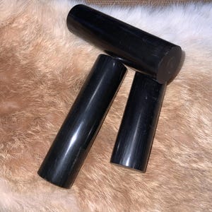 May include: Three black cylindrical objects made of polished wood. The objects are arranged in a triangular shape on a light brown fuzzy surface.