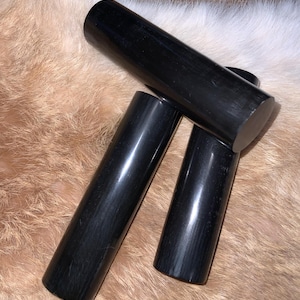 May include: Three black polished cylindrical objects, possibly made of wood or stone, are arranged on a white furry surface.