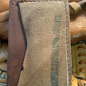 Cartera de cuero con forma de guante de béisbol. Fabricada con guantes de béisbol reciclados y piel de novillo de primera calidad. Tiene 3 bolsillos. Fabricada en Estados Unidos.