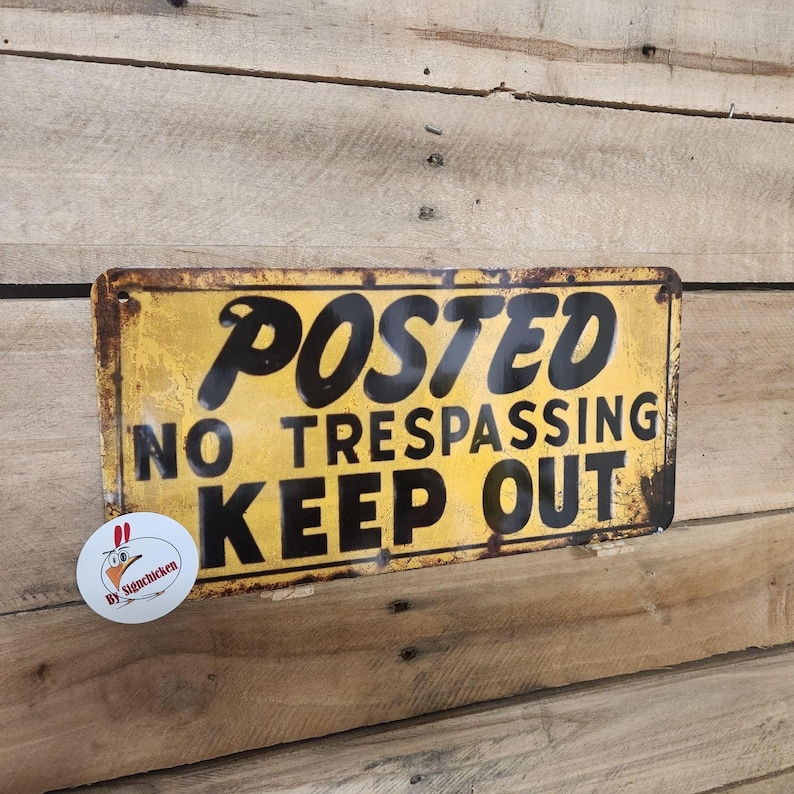 May include: A yellow metal sign with black text that reads "POSTED NO TRESPASSING KEEP OUT". The sign has a distressed, rusty look.