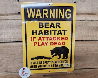 May include: Yellow warning sign with black text that reads "WARNING BEAR HABITAT IF ATTACKED PLAY DEAD IT WILL BE GREAT PRACTICE FOR WHEN YOU DIE IN A FEW MINUTES". A black silhouette of a bear is shown attacking a person.