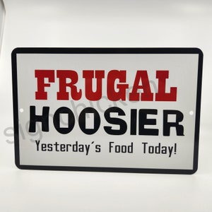 Puede incluir: Un letrero de metal blanco con letras negras y rojas. El letrero dice "Frugal Hoosier Yesterday's Food Today!"