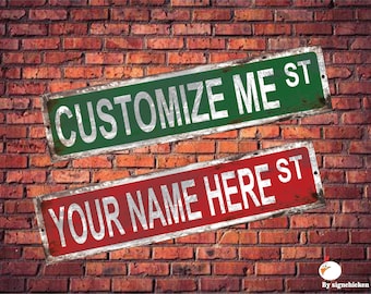 May include: Two metal street signs with distressed paint. The top sign is green with white text that reads "CUSTOMIZE ME ST". The bottom sign is red with white text that reads "YOUR NAME HERE ST".