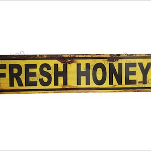 May include: A yellow metal sign with a distressed, rusty finish. The sign reads "FRESH HONEY" in black letters.