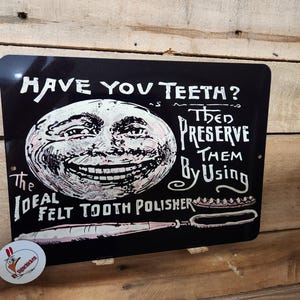 Pode incluir: Placa de metal preta com texto branco e um rosto de lua sorrindo. A placa diz "HAVE YOU TEETH? THEN PRESERVE THEM BY USING THE IDEAL FELT TOOTH POLISHER." Um anúncio dentário vintage.