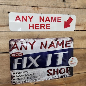 Könnte beinhalten: Zwei Metallschilden mit einem abgenutzten Look. Das obere Schild ist weiß mit rotem Text, der "ANY NAME HERE" sagt, mit einem roten Pfeil, der nach unten zeigt. Das untere Schild ist blau, rot und weiß mit dem Text "ANY NAME FIX IT SHOP" und den Worten "OLD SCHOOL" und "ALWAYS OPEN".