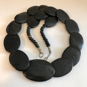 May include: A black necklace made of large oval-shaped beads. The necklace is made of a smooth, polished material and has a simple, elegant design.