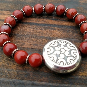 May include: A red gemstone bracelet with a silver charm featuring a decorative design. The bracelet is made of round beads with silver accents.